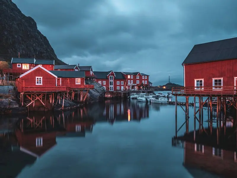 Stunning view of red stilt houses reflecting in the water at Å i Lofoten during twilight.