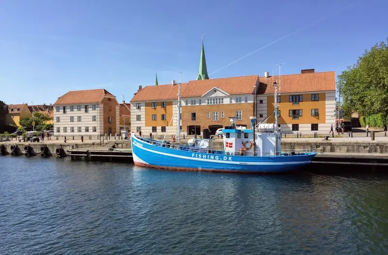 A vibrant blue fishing boat moored at Helsingør harbor with historic buildings in the background.