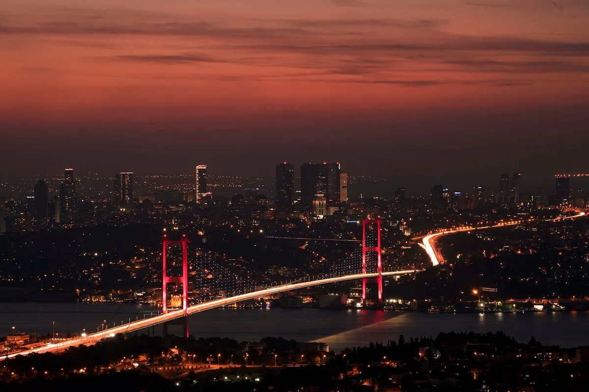 Stunning night view of the illuminated Bosphorus Bridge and Istanbul skyline under a red sky.
