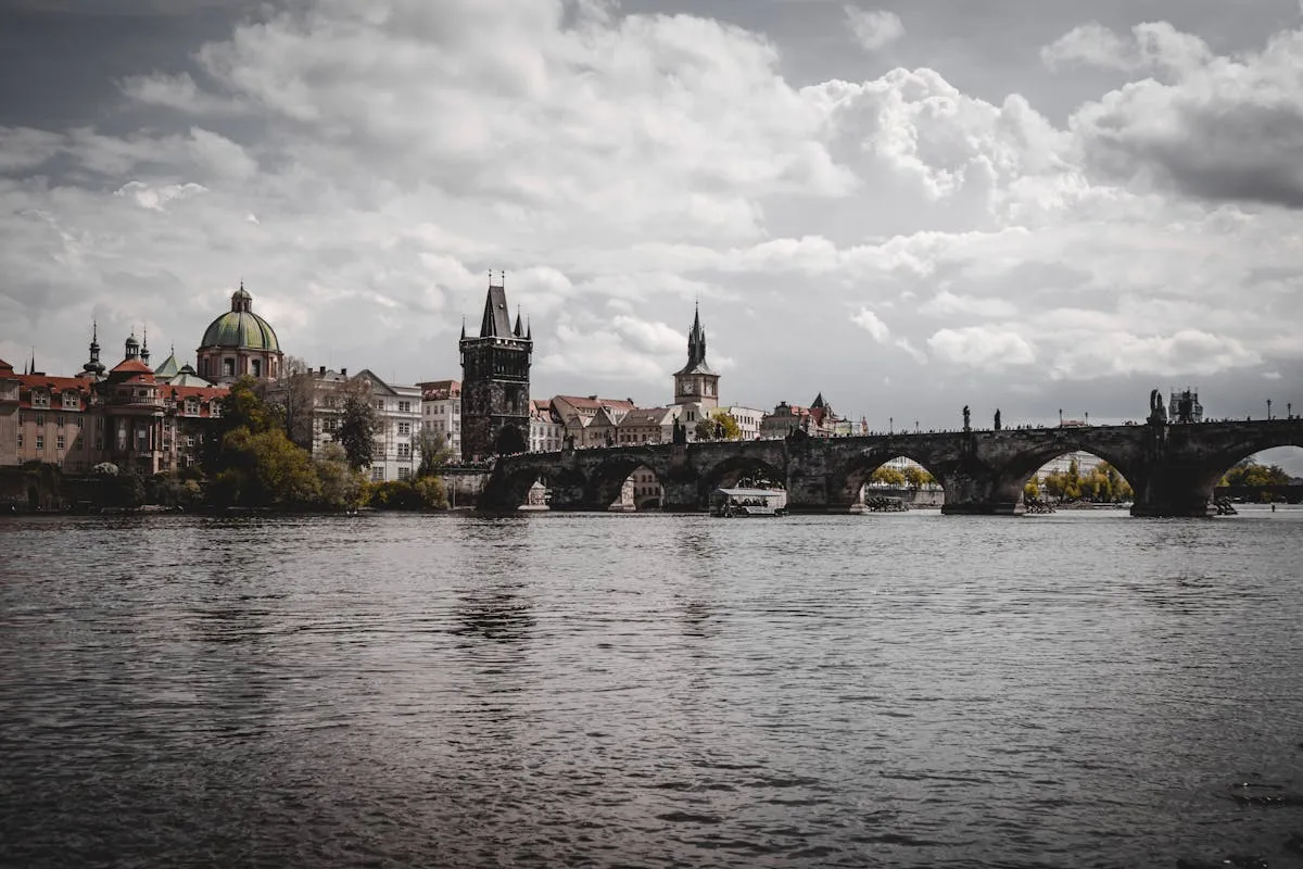 Iconic view of Charles Bridge spanning Vltava River with Prague's skyline, cloudy skies.