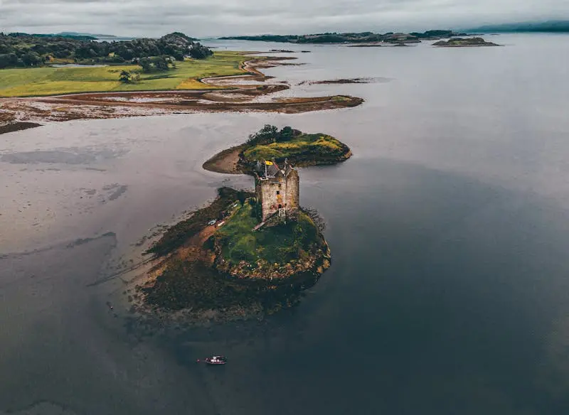 Aerial shot of Castle Stalker on Loch Laich, depicting a moody landscape in Argyll and Bute, Scotland.