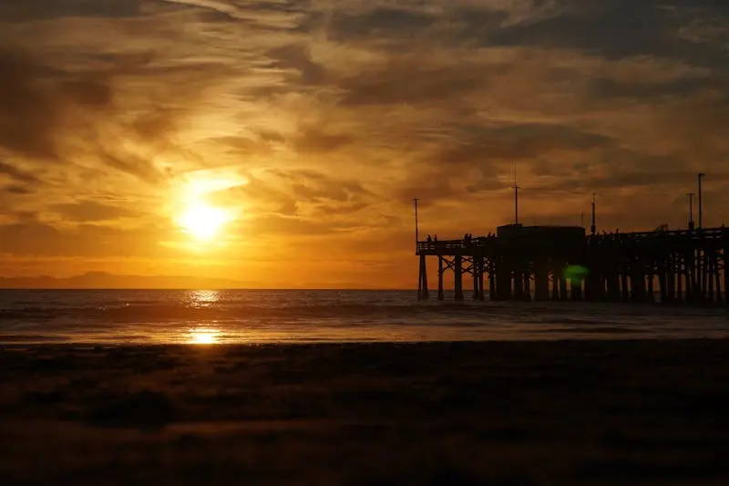 Golden sunset over Newport Beach pier with crashing waves and a vibrant sky.