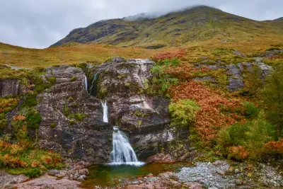 A stunning waterfall in the Scottish Highlands amidst autumn foliage and rugged landscape.