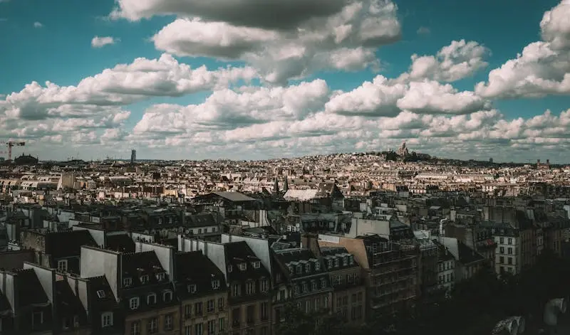 Panoramic view of Paris rooftops with dramatic clouds, showcasing classic architecture.
