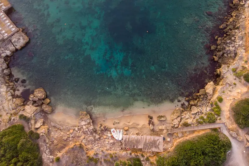 Drone shot of a rocky beach cove with crystal clear water and a small dock. Perfect for travel and nature concepts.