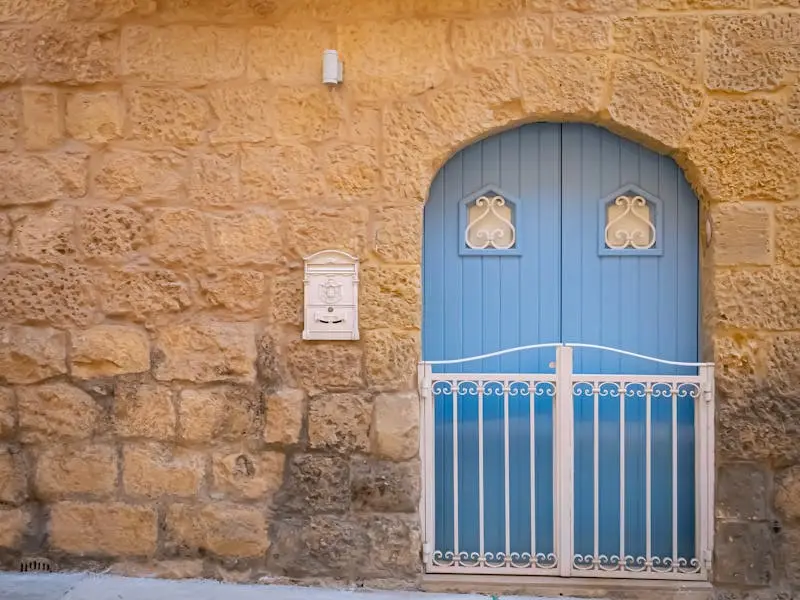 A picturesque blue arched door set in a traditional stone facade in Malta's historic streets.
