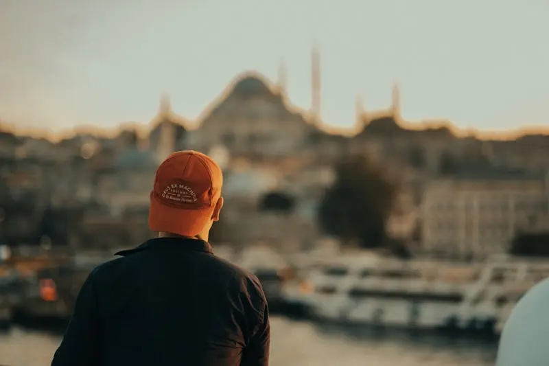 A man wearing a cap gazes at the Istanbul skyline and Hagia Sophia, capturing the city's essence at sunset.