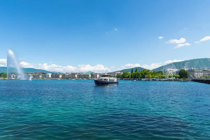 Beautiful view of Lake Geneva featuring the Jet d'Eau and a Ferris wheel under a sunny blue sky.