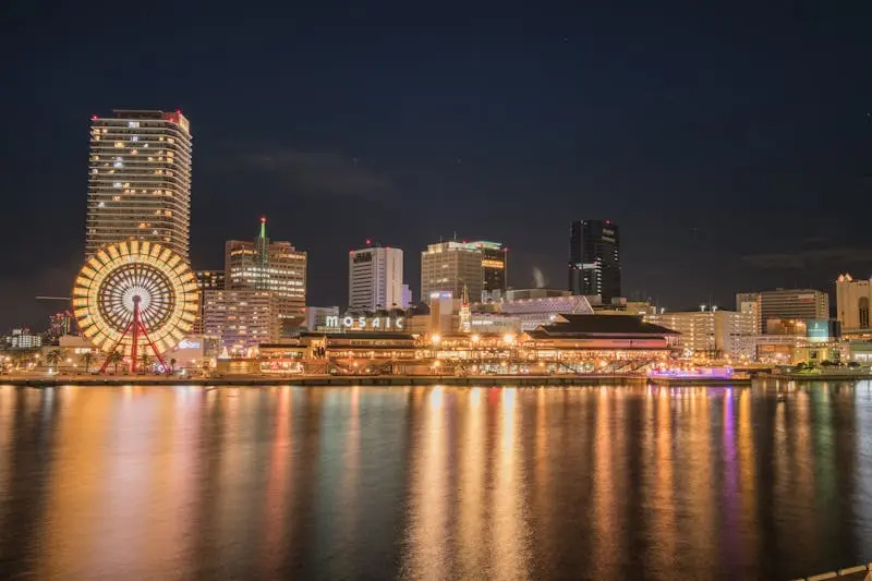 Stunning night cityscape of Kobe with illuminated Ferris wheel reflecting on the waterfront.