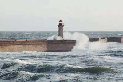 Lighthouse at Porto's coastline with waves crashing on a sunny day, creating a dramatic ocean scene.