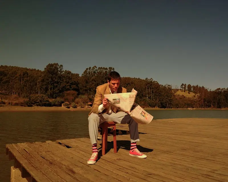 Man reading a newspaper outdoors on a lakeside dock in Serra Negra, Brazil.