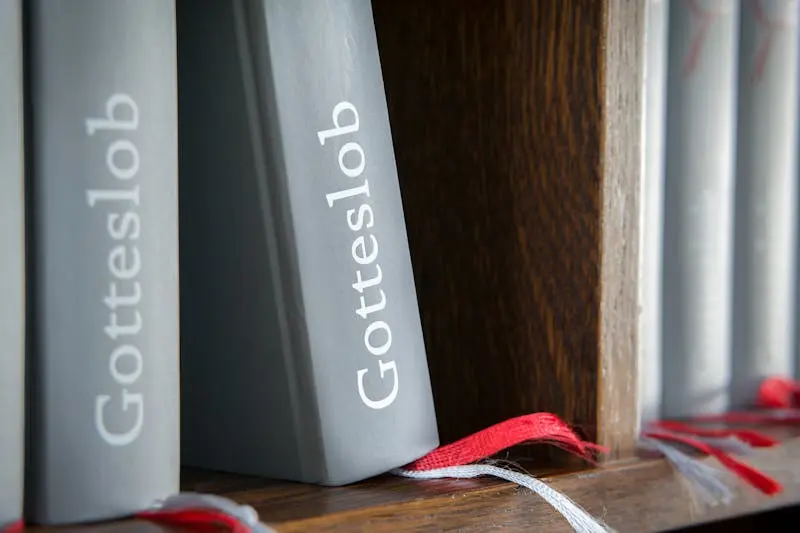 Close-up of Gotteslob hymn books with red bookmarks on wooden shelf.