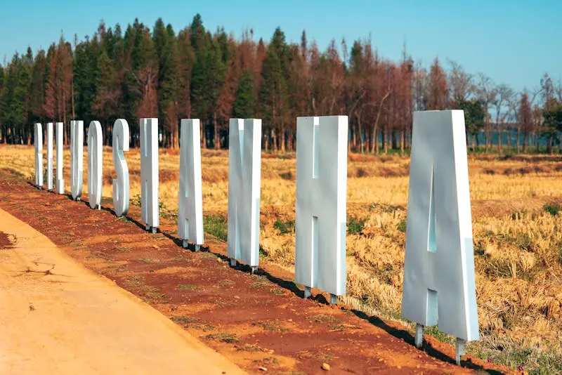 3D letters spelling 'LUOSHAN' in a field with pine trees, clear skies, and sunlight.