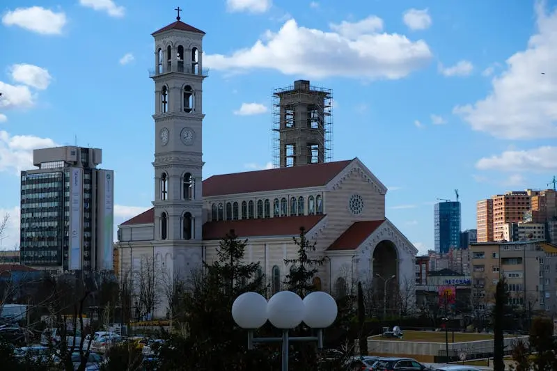 Catholic Cathedral surrounded by modern cityscape in Pristina, an architectural landmark blending past and present.