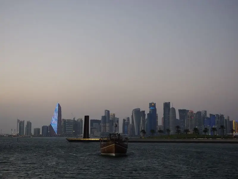 Scenic view of Doha city skyline with traditional dhow boat at dusk along the waterfront.