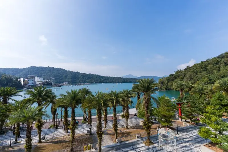Beautiful view of Sun Moon Lake with palm-lined walkways, blue skies, and serene waters.