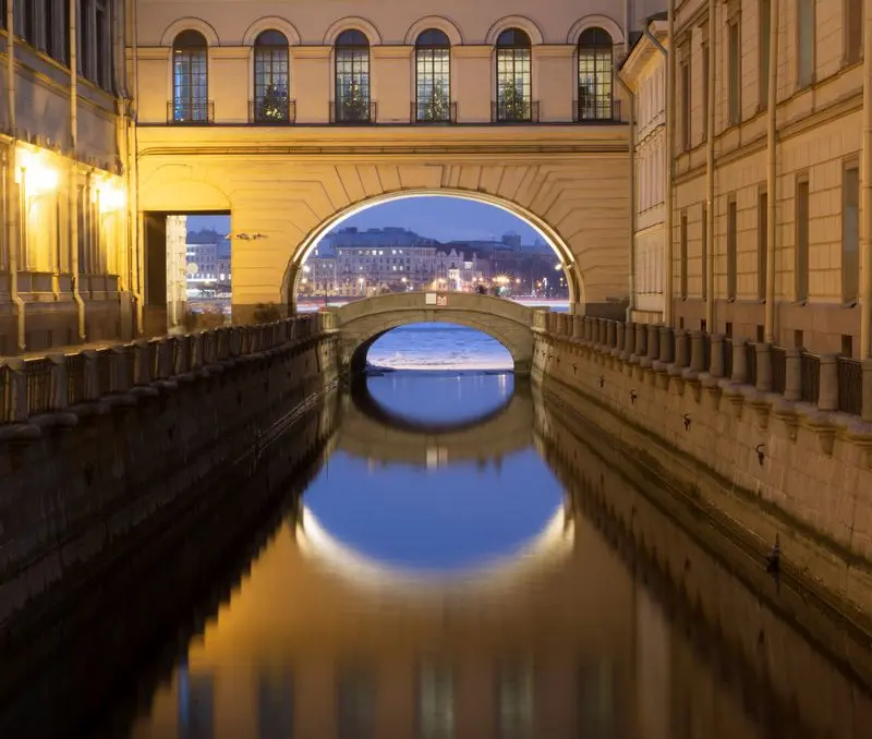 Beautiful view of a historic canal and bridge in Saint Petersburg at twilight, reflecting city lights.
