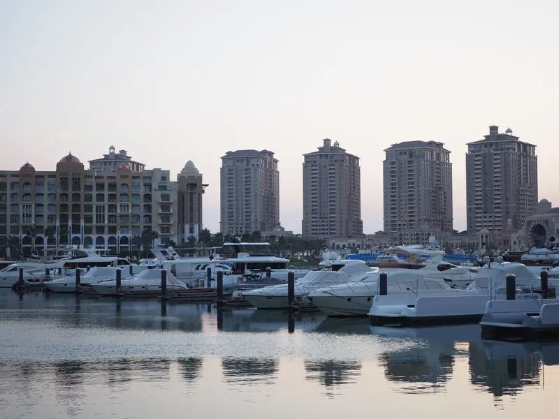 Beautiful evening view of luxury yachts at a marina in Doha, Qatar with tall buildings in the background.