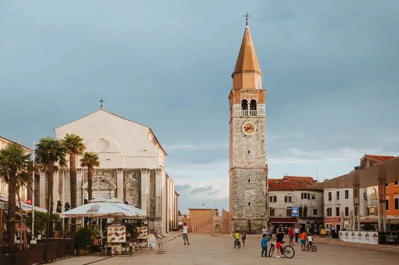 Picturesque street scene in Chorvátsko featuring a historic church and bell tower under a blue sky.