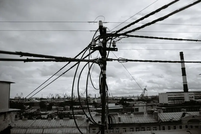 Black-and-white view of tangled power lines against an urban industrial landscape with cranes.