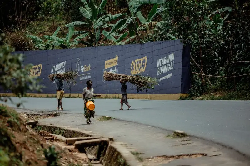 Three individuals walking along a road carrying firewood atop their heads.
