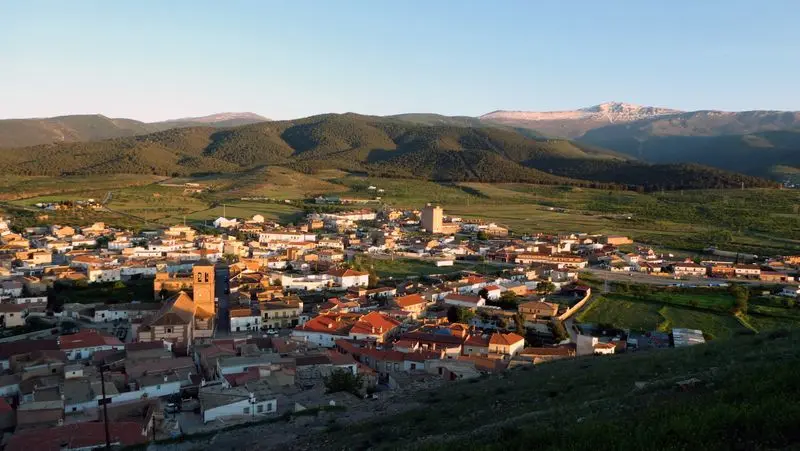 A breathtaking aerial view of a serene village nestled in lush mountains under a clear sky at sunset.