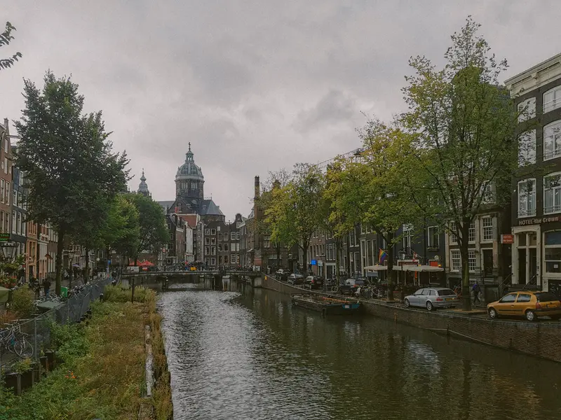Scenic view of Amsterdam's canal with historic buildings and cathedral on a cloudy day.